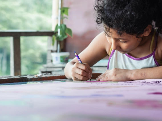 A child holds a pen and leans over a piece of paper.