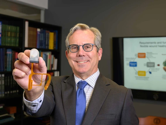 A person holds a small grey wearable device used for would healing