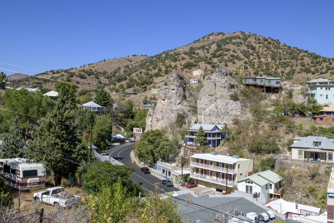 Looking down at the town of Bisbee, Arizona, showing main road, houses, hotel, store, with mountains in background.