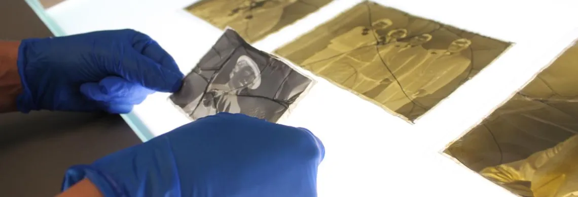 an old corroded photo negative is being examined by an art conservator with gloves on over a light box 